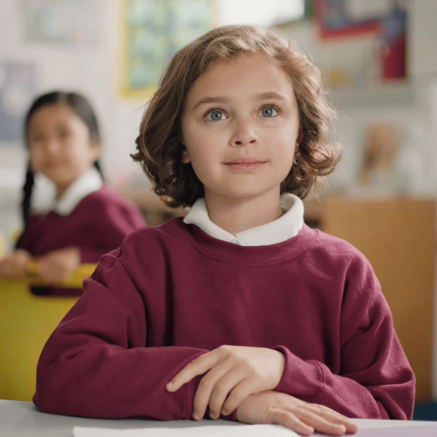 child sat in uniform at desk in school