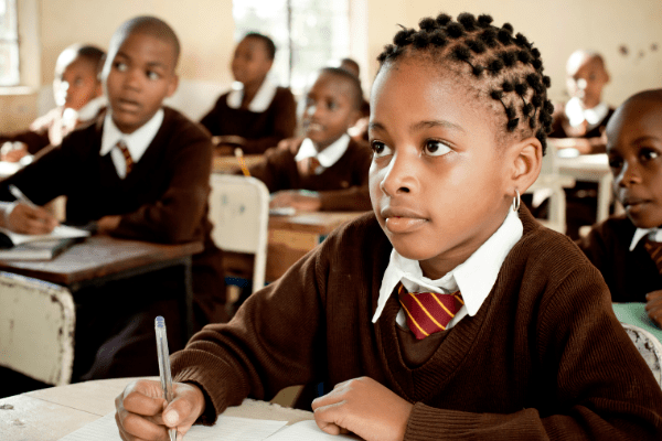 child in uniform holding pen sat at desk in class