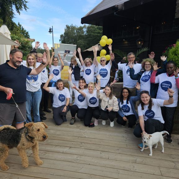 Group photo of CAWS and Legal Eagles volunteers cheering outside, with some wearing white t-shirt's with the Citizens Advice West Sussex logo. Two dogs also feature in the front of the photo.