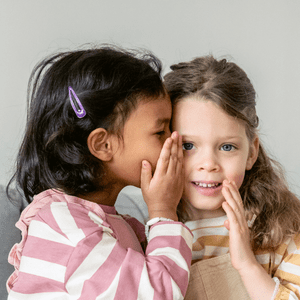 2 little girls in pink, 1 whispering in the other's ear. Shared services.