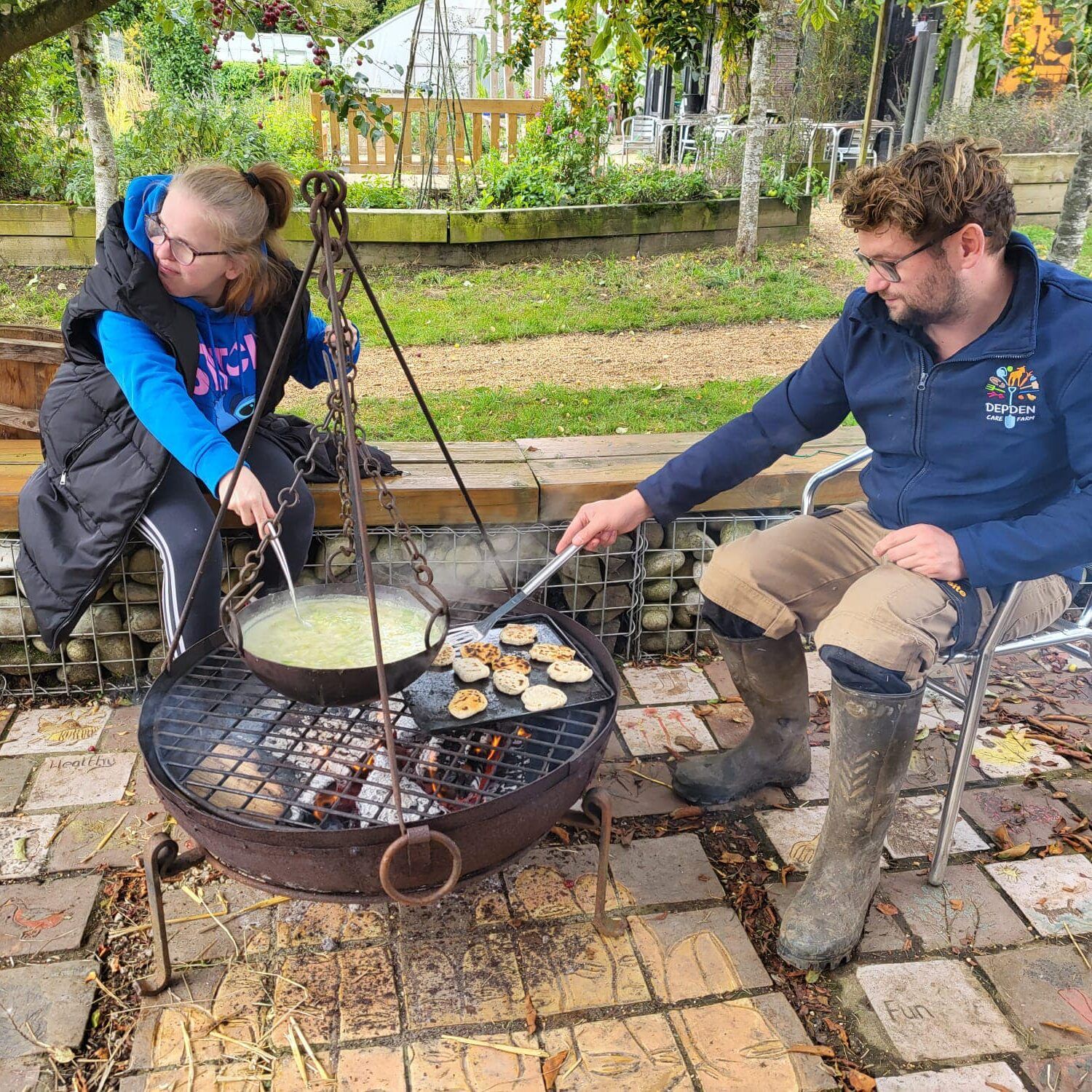 Millennium Farm Trust 2 people cooking on an open fire with a big hanging pot