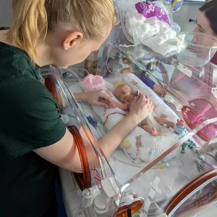 Neonatal care unit in a hospital with a nurse in a green outsite and a tiny baby in an incubator. Bliss charity.