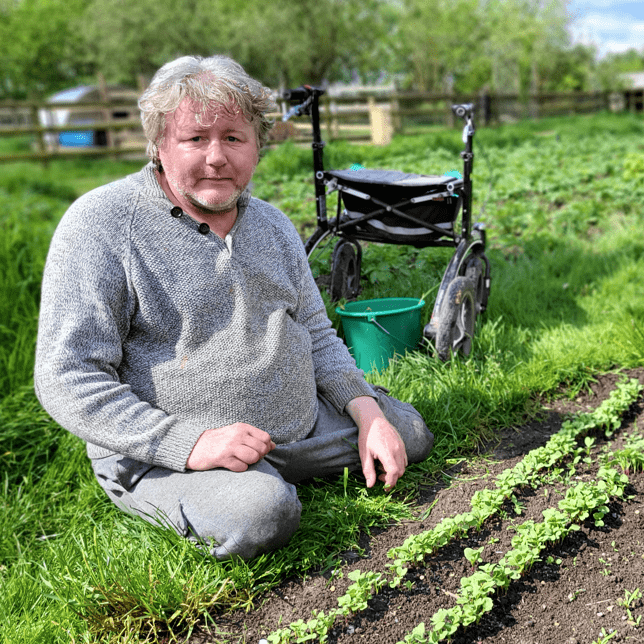 Millennium Farm Trust man in grey tracksuit planting seedlings