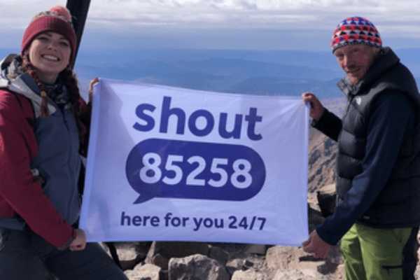 Jonathan_and_Faye standing on top of a mountain with a Shout 84258 flag. fundraising for Shout The Mix and MHI merger case study 2
