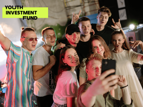Youth Investment Fund Partner Post with logo and a photo of 9 young people posing for a selfie on a theatre stage