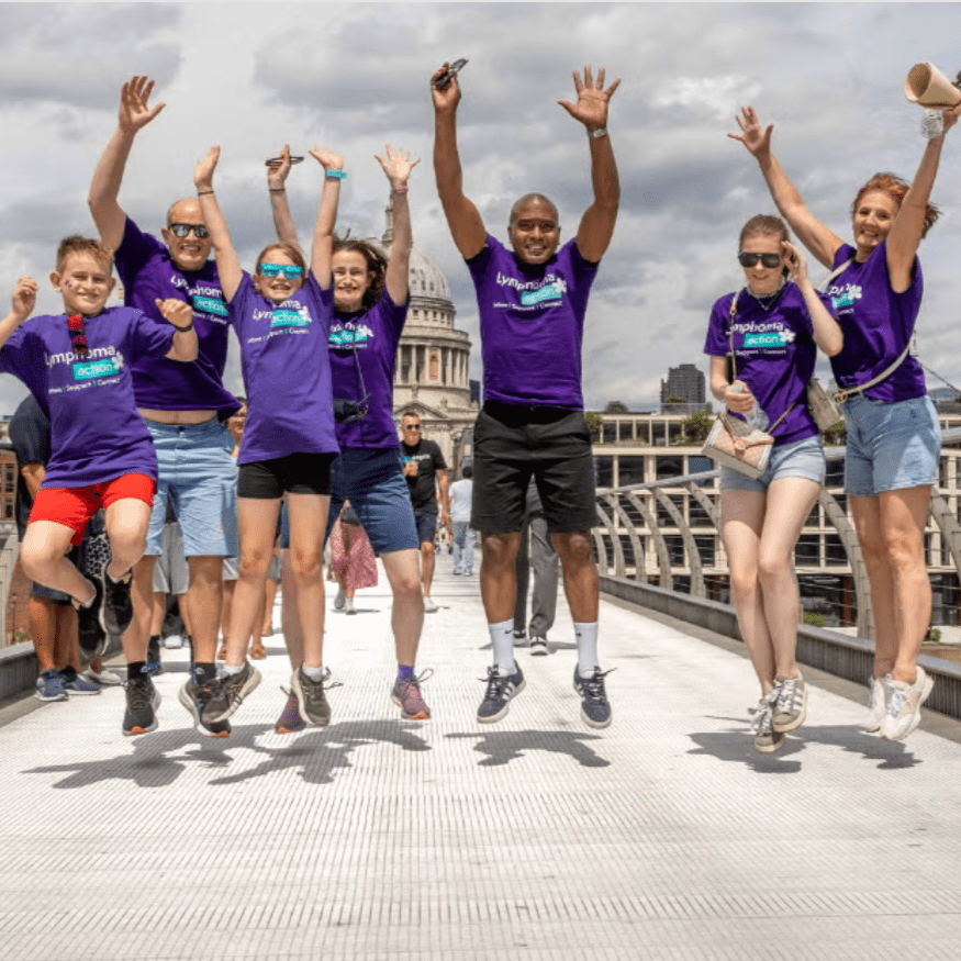 Lymphoma Action volunteers jumping in the air on a bridge walk wearing purple t-shirts.