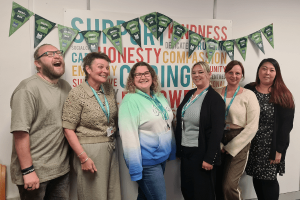 Nurtrio merger case study, 6 people standing in front of bunting and a word cloud with words including support, kindness and caring