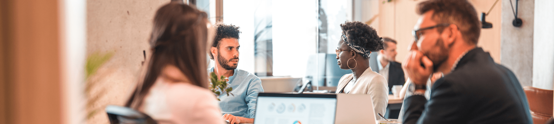 5 peopel sitting at desks in a modern office. 1 black lady with big hooped earrings, 2 men with beards, 1 lady with long hair