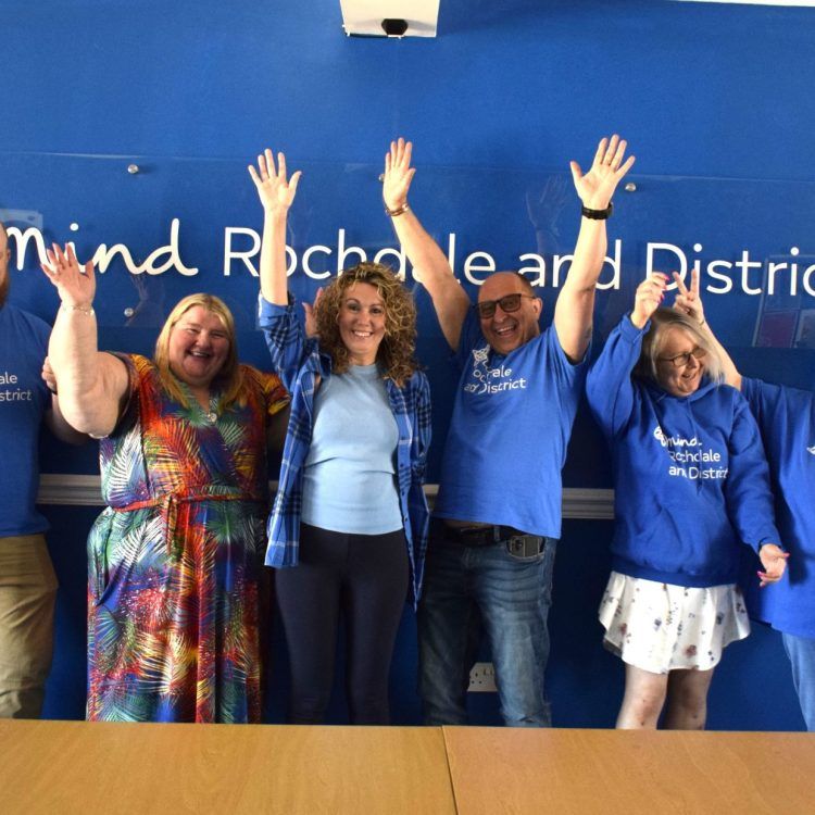 Rochdale and District Mind volunteers, 1 man and 1 woman wearing blue Mind tshirts, then 2 more women wearing their own clothes, with all 4 cheering with hands in the air