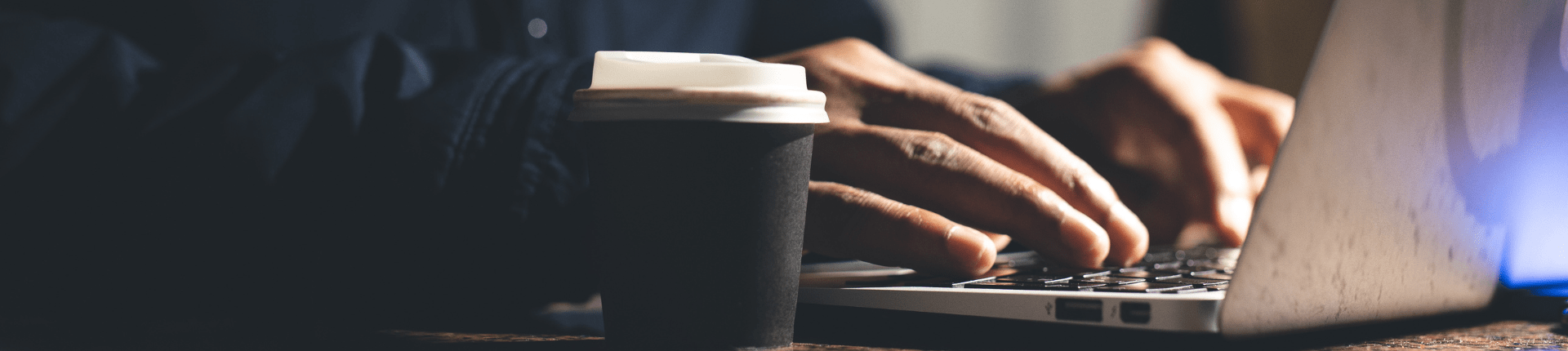 Financial Crime & data protection a man's hands typing on a laptop keyboard and a takeaway cup of coffee