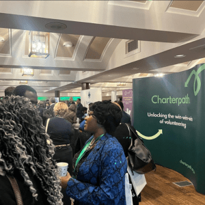 Charterpath event with lady standing talking to others in front of a Charterpath stand, holding a cup.