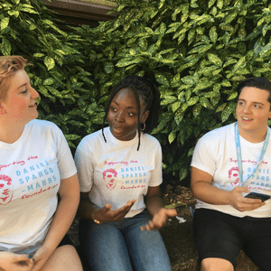 3 DSM Foundation youth ambassadors volunteers sitting outside talking wearing white DSM tshirts.