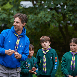 Greater Manchester East Scouts adult leader with young children smiling and wearing green scout uniform.