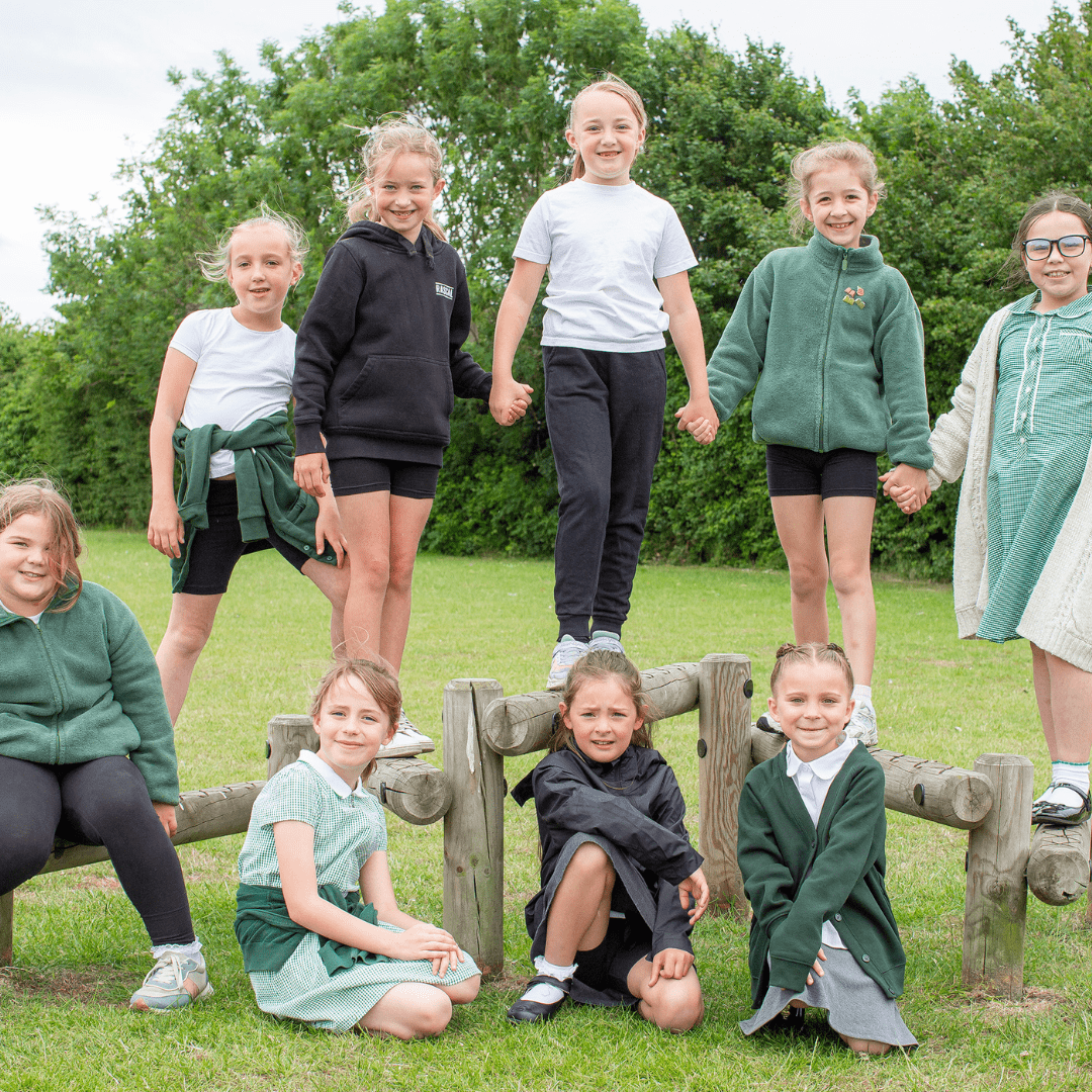 9 girls from South Essex Academy Trust standing on wooden fence holding hands and some standing in front of the fence wearing a mix of green, navy and white.