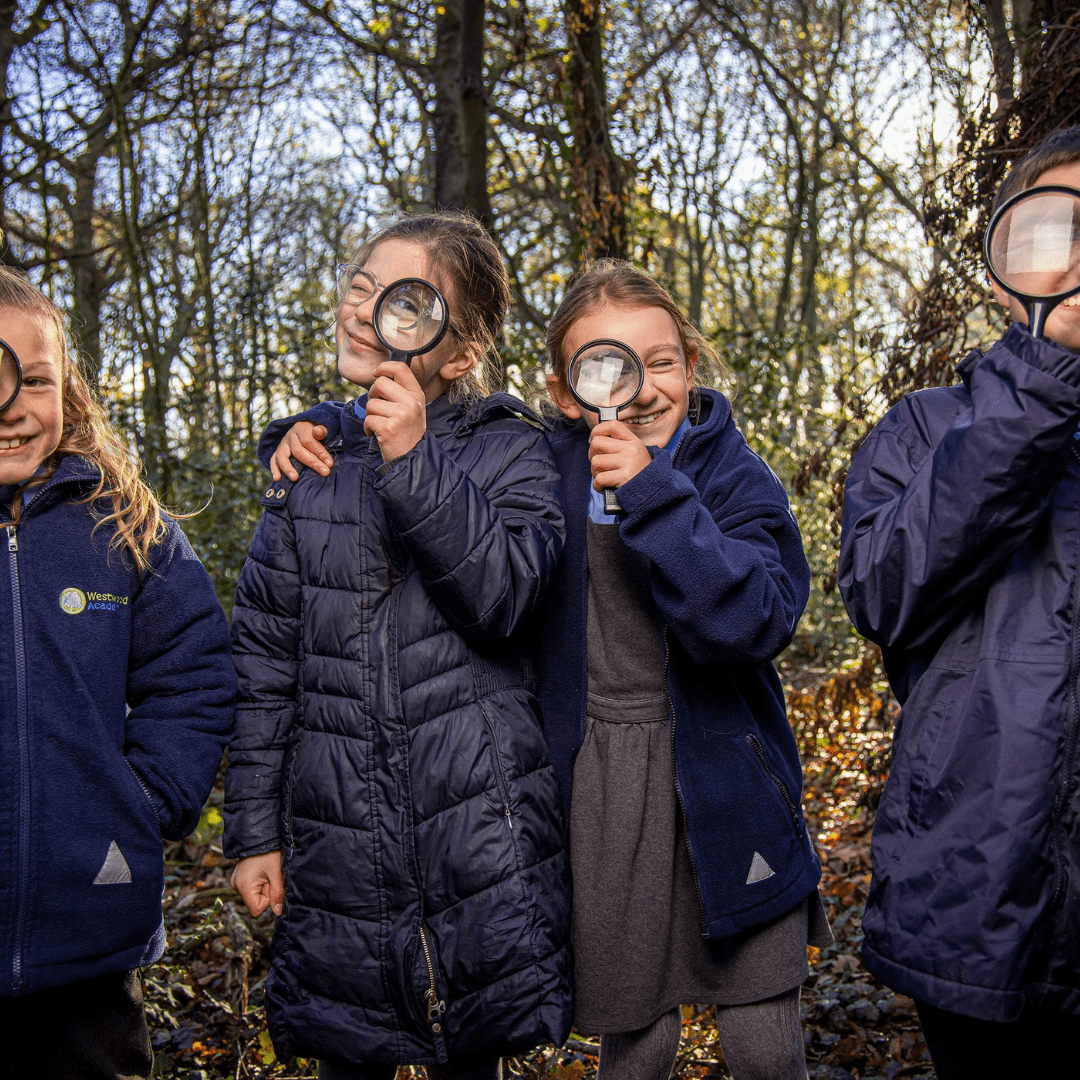 Four South East Academy Trust children stood outside in front of trees holding magnifying glasses.